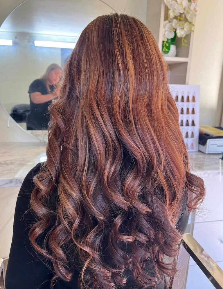 Back view of woman with long wavy copper-brown hair with highlights in a hair salon setting
