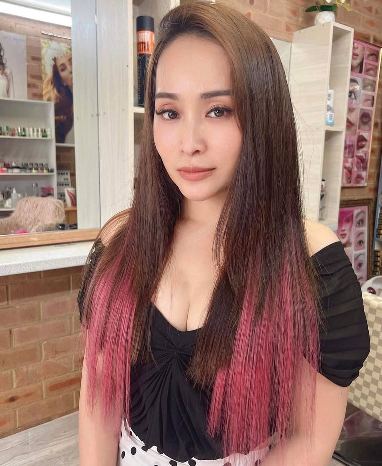 Woman with long brunette hair featuring pink ombre tips, wearing a black top in a salon setting