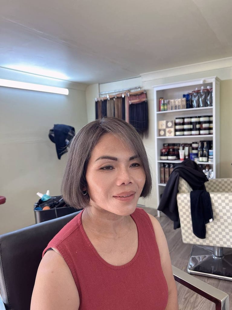 Woman with shoulder-length gray hair wearing a maroon sleeveless top, smiling in a bedroom with shelving and clothing visible in background