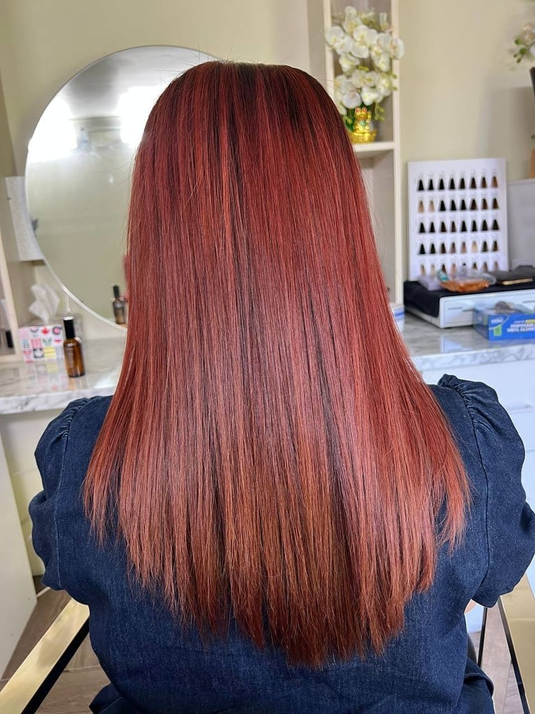 Back view of a woman with long, straight auburn hair in a salon setting with mirror and nail polish display
