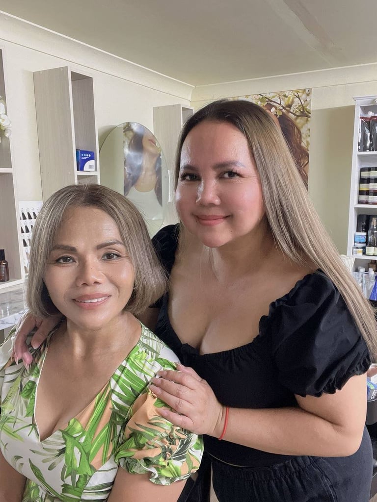 Two women smiling at camera in home interior, one wearing green floral top and one in black shirt