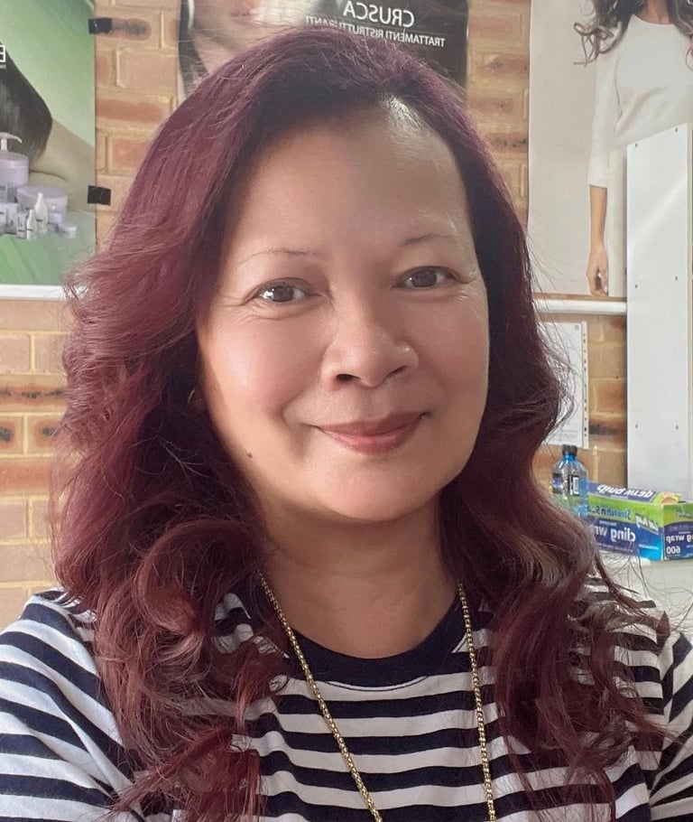 Portrait of a woman with burgundy wavy hair wearing a striped black and white shirt and gold chain necklace, smiling indoors