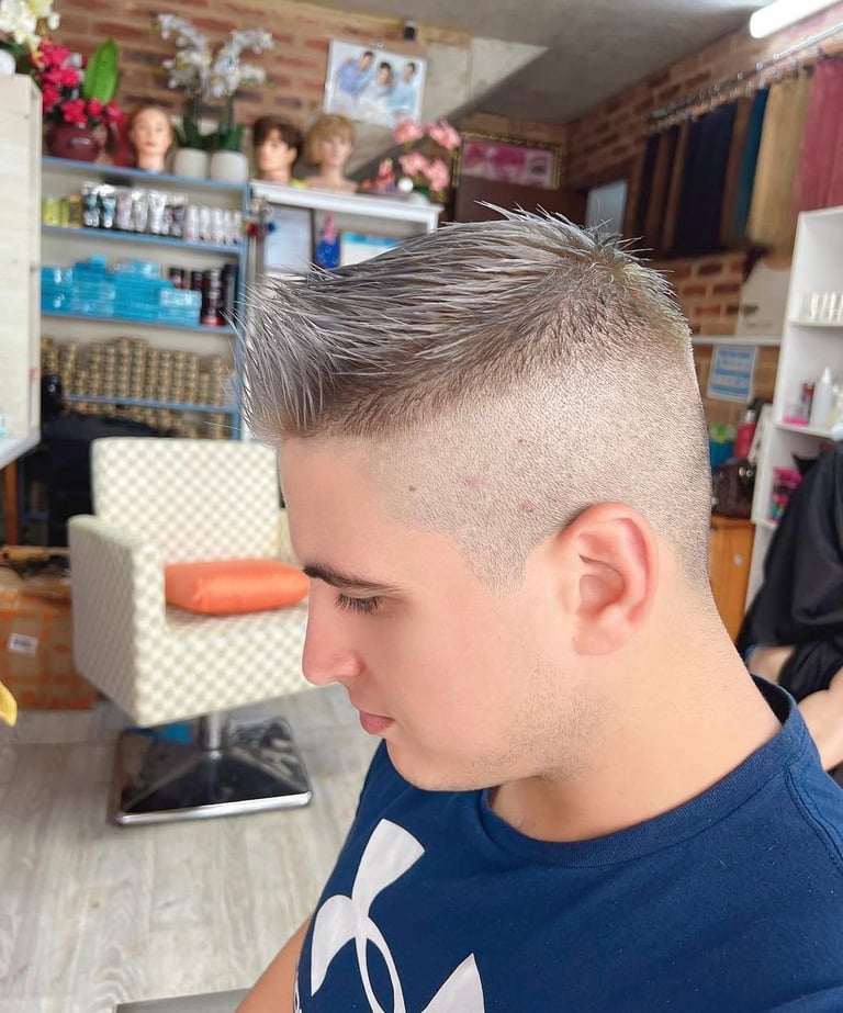 Young man with a modern undercut hairstyle, short sides and longer textured top, wearing a dark blue shirt in a salon setting