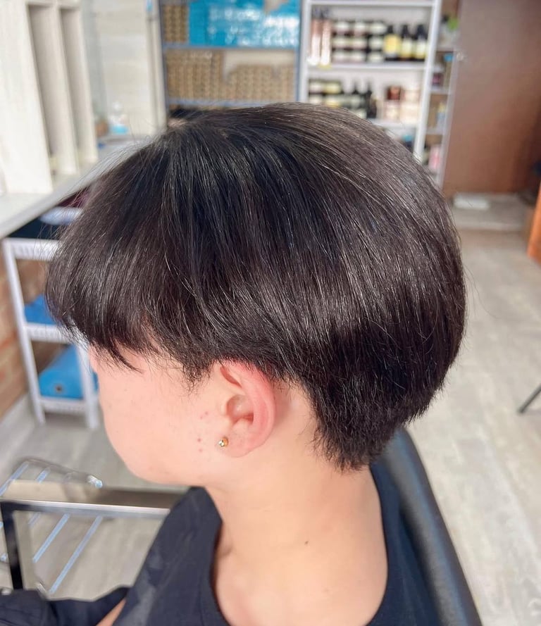 Side profile of a person with a short dark pixie haircut in a salon setting
