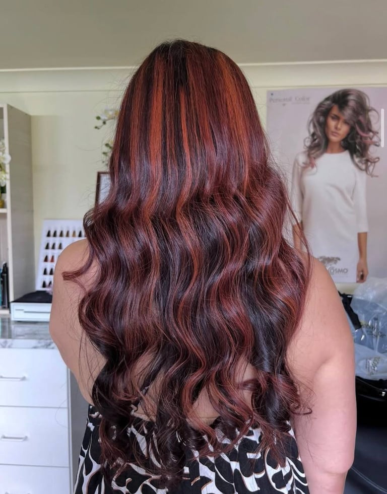 Back view of woman with long burgundy wavy hair in a salon setting